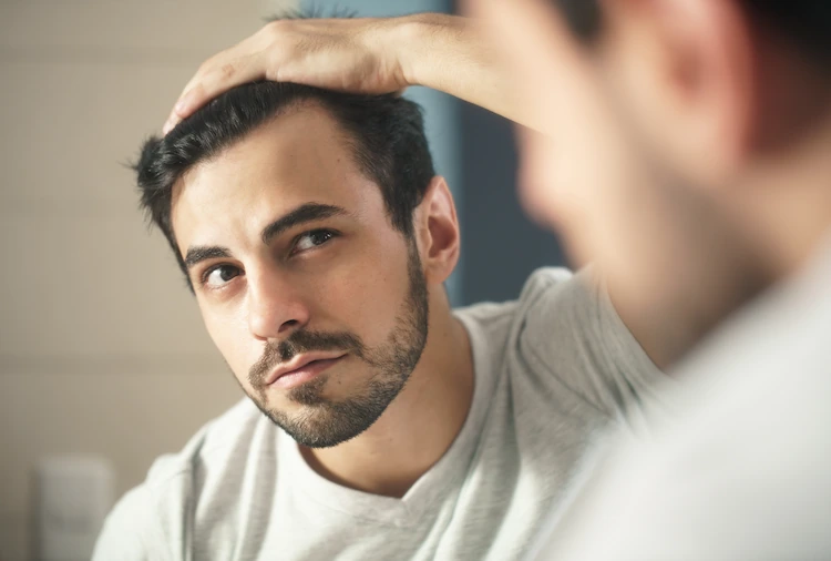 Man looking in the mirror to examine hair loss after bariatric surgery